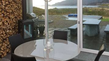 A dining area with a round table, chairs, a grill, and a view of a lake and mountains.
