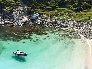 A boat on clear turquoise water near a rocky shoreline with dense greenery in the background.