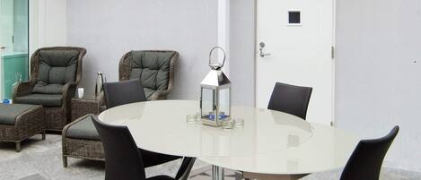 Een vergaderruimte met een glazen tafel, vier zwarte stoelen, twee rieten stoelen, een witte deur en een vloerkleed met stervenspatroon.