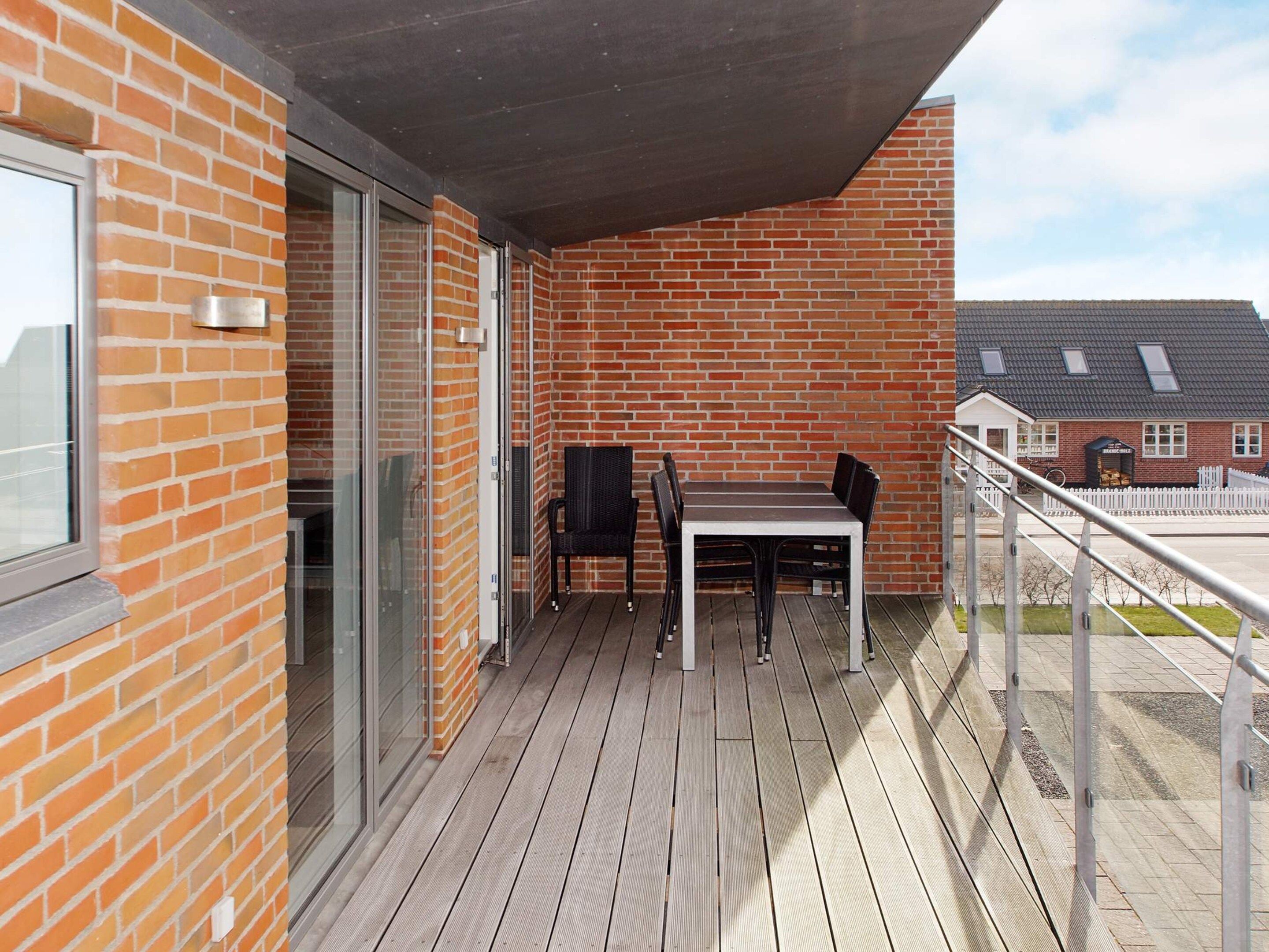 Un balcón con piso de madera, una mesa con sillas y un muro de ladrillo.