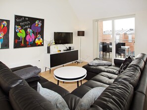 A modern living room with a black leather sofa, a white round coffee table, and a flat-screen TV on a black and white entertainment unit. - 4 Star Holiday Home in Hemmet (Hemmet)