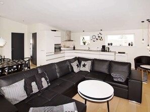 A modern living room with a black leather sectional sofa, a round coffee table, and a dining area with a black tablecloth. - 4 Star Holiday Home in Hemmet (Hemmet)