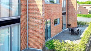 Un bâtiment moderne avec une façade en briques, de grandes fenêtres et un patio doté d’un espace extérieur aménagé avec des sièges.