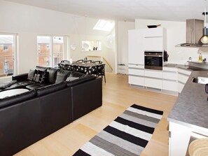 A modern living room with a black leather sofa, a dining table with chairs, and a kitchen area with white cabinets and a stainless steel sink. - 4 Star Holiday Home in Hemmet (Hemmet)