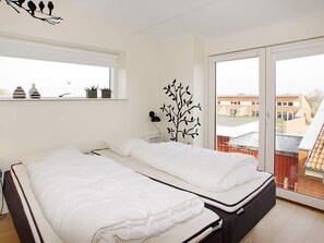 A bedroom with two beds, a window with plants, a wall-mounted lamp, and a view of buildings outside. - 4 Star Holiday Home in Hemmet (Hemmet)