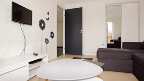 Un salon moderne doté d’un téléviseur à écran plat, d’une table blanche, d’un canapé de couleur foncée et d’œuvres d’art décoratives accrochées au mur.
