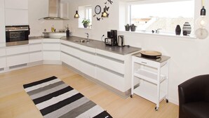 Une cuisine moderne avec des meubles blancs, un four encastré, une machine à café et une fenêtre agrémentée de plantes.