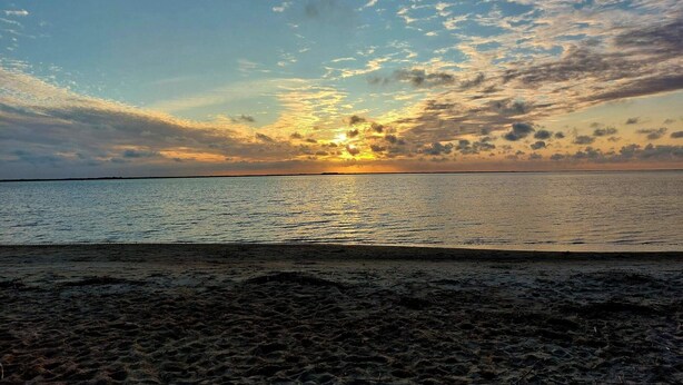 Une plage avec un coucher de soleil sur l’eau.