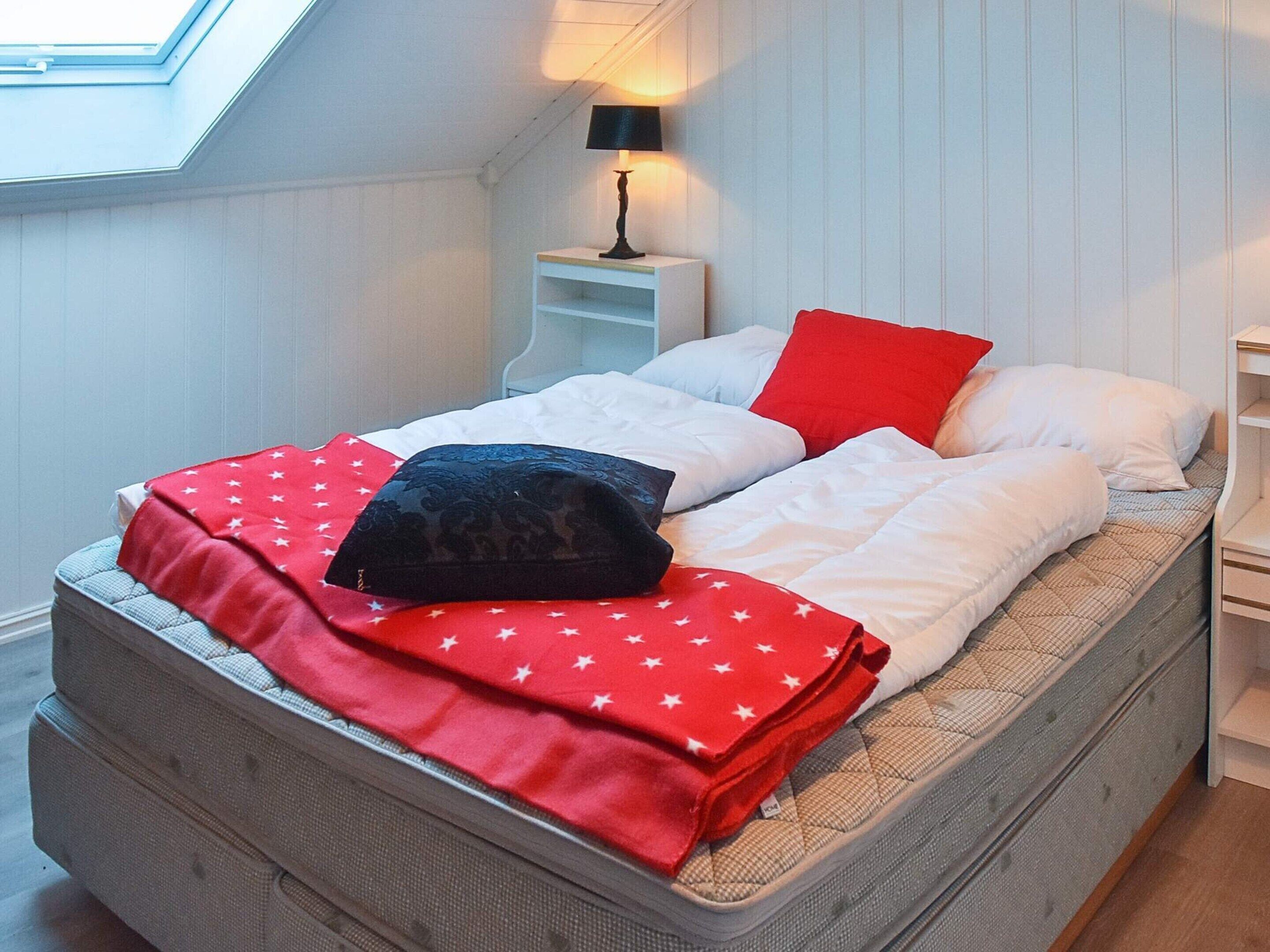 A bedroom with a bed, a nightstand, a lamp, and a skylight.