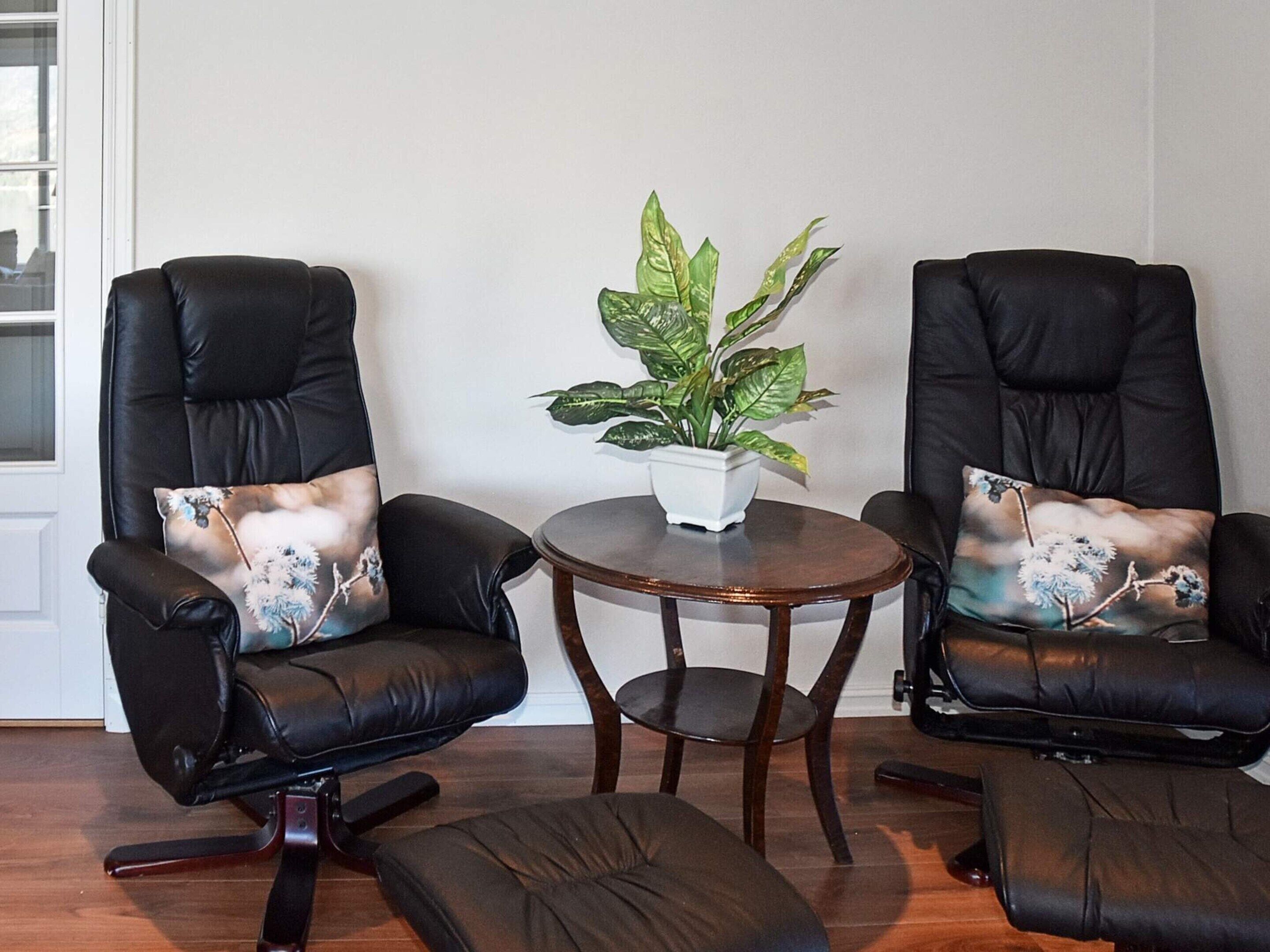 Two black leather armchairs with floral cushions, a small round wooden table, and a potted plant between them.