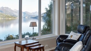 Una habitación con vistas a un lago y montañas, un sofá de cuero, una pequeña mesa de madera y una lámpara.