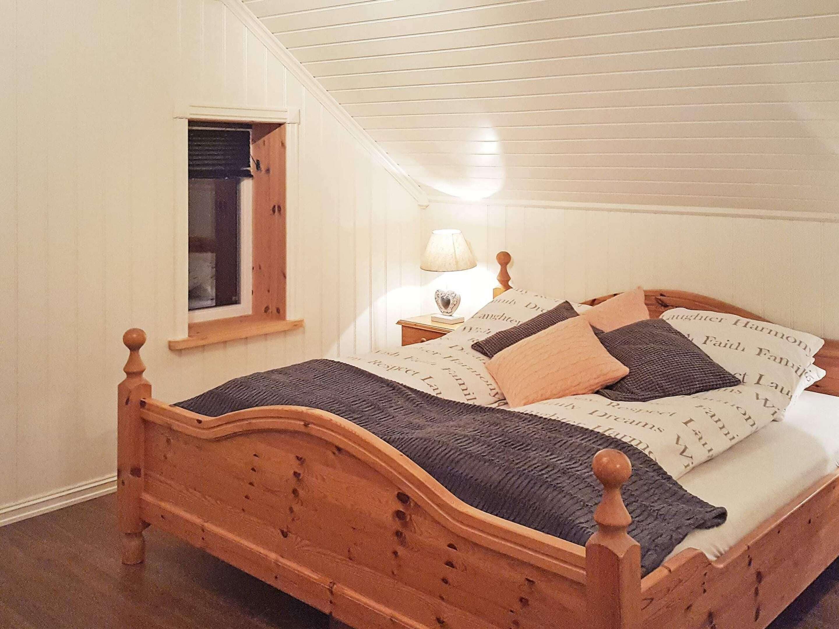 A wooden bed with a headboard, a bedside table with a lamp, and a window with a view.