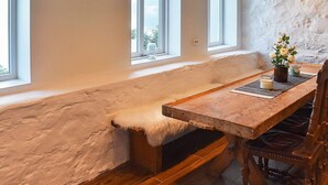 Una habitación con techos altos, una mesa de madera y un banco, ventanas grandes y una pared de piedra rústica.