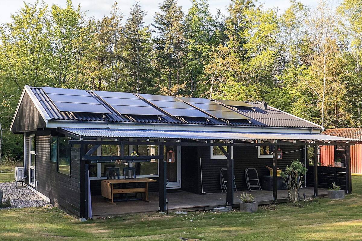 A modern log cabin with a covered porch, solar panels, and a small outdoor seating area.