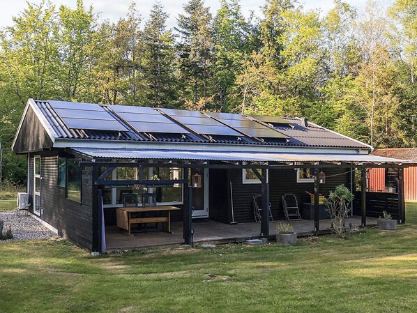 A modern log cabin with a covered porch, solar panels, and a small outdoor seating area.