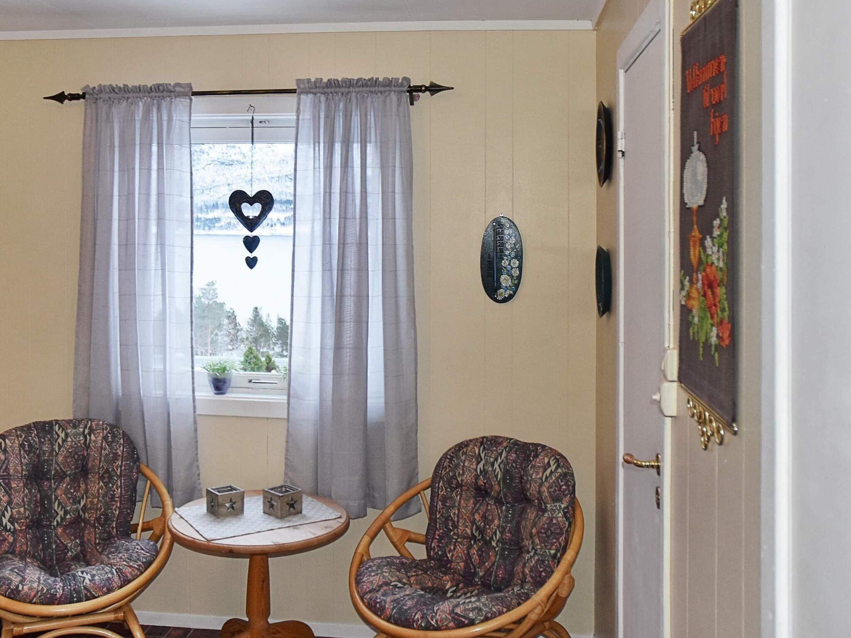 A room with two wicker chairs, a small round table, a window with curtains, and a door with a poster.