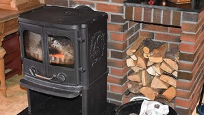 A wood-burning stove with a glass door, a brick fireplace, and a bucket of ashes. - 8 Person Holiday Home in Eidsvag (Molde)