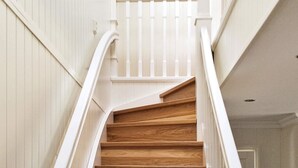 Una escalera de madera con barandillas blancas y una pared blanca.
