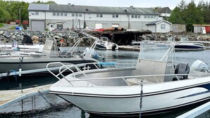 Un puerto deportivo con varias embarcaciones amarradas, un edificio al fondo y un litoral rocoso.