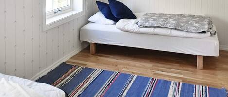 A single bed with a white mattress and blue pillows, a gray blanket, and a striped rug on a wooden floor.