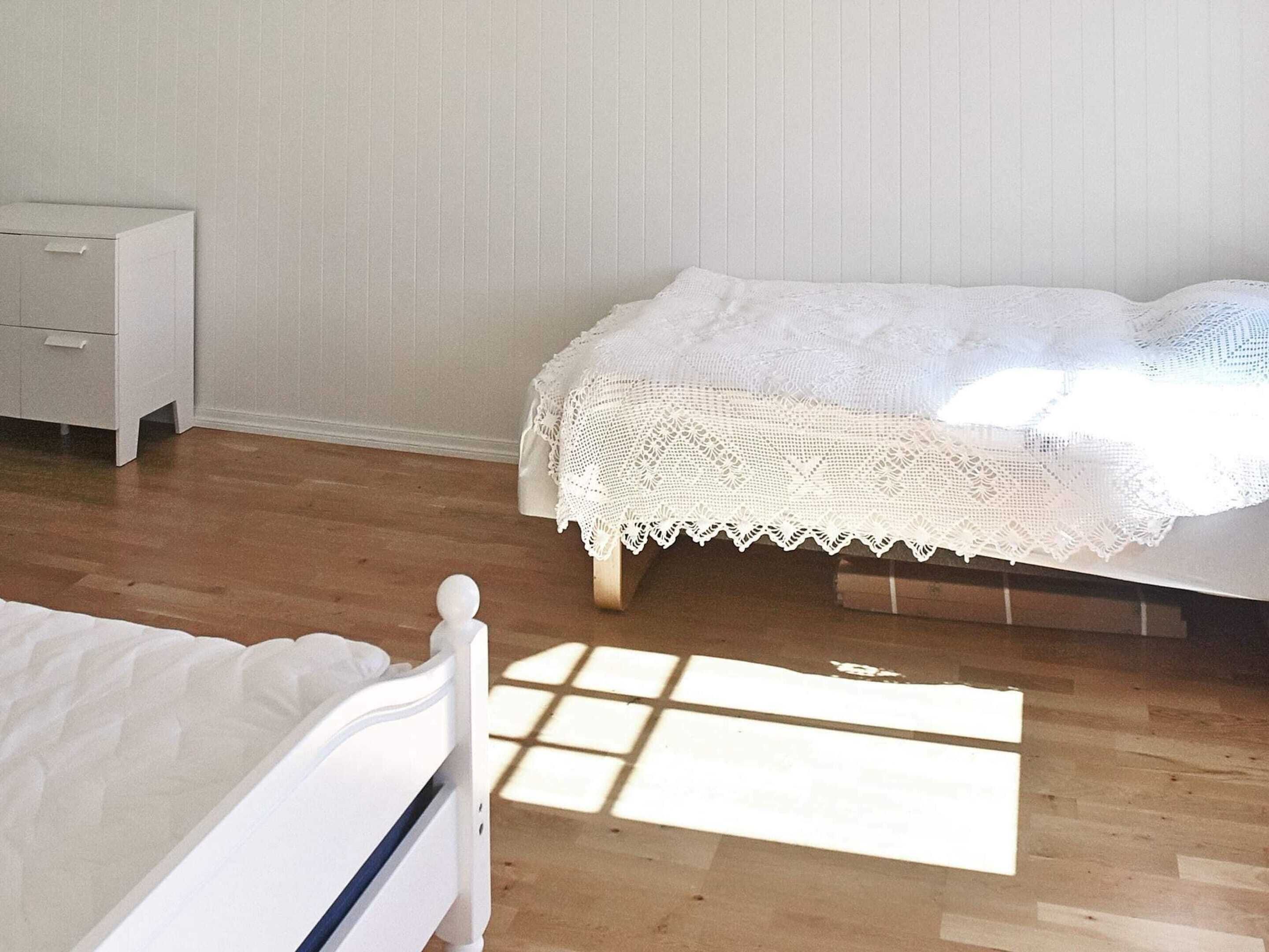 A bedroom with a wooden floor, a white bed with a white headboard, a white nightstand, and a white dresser.