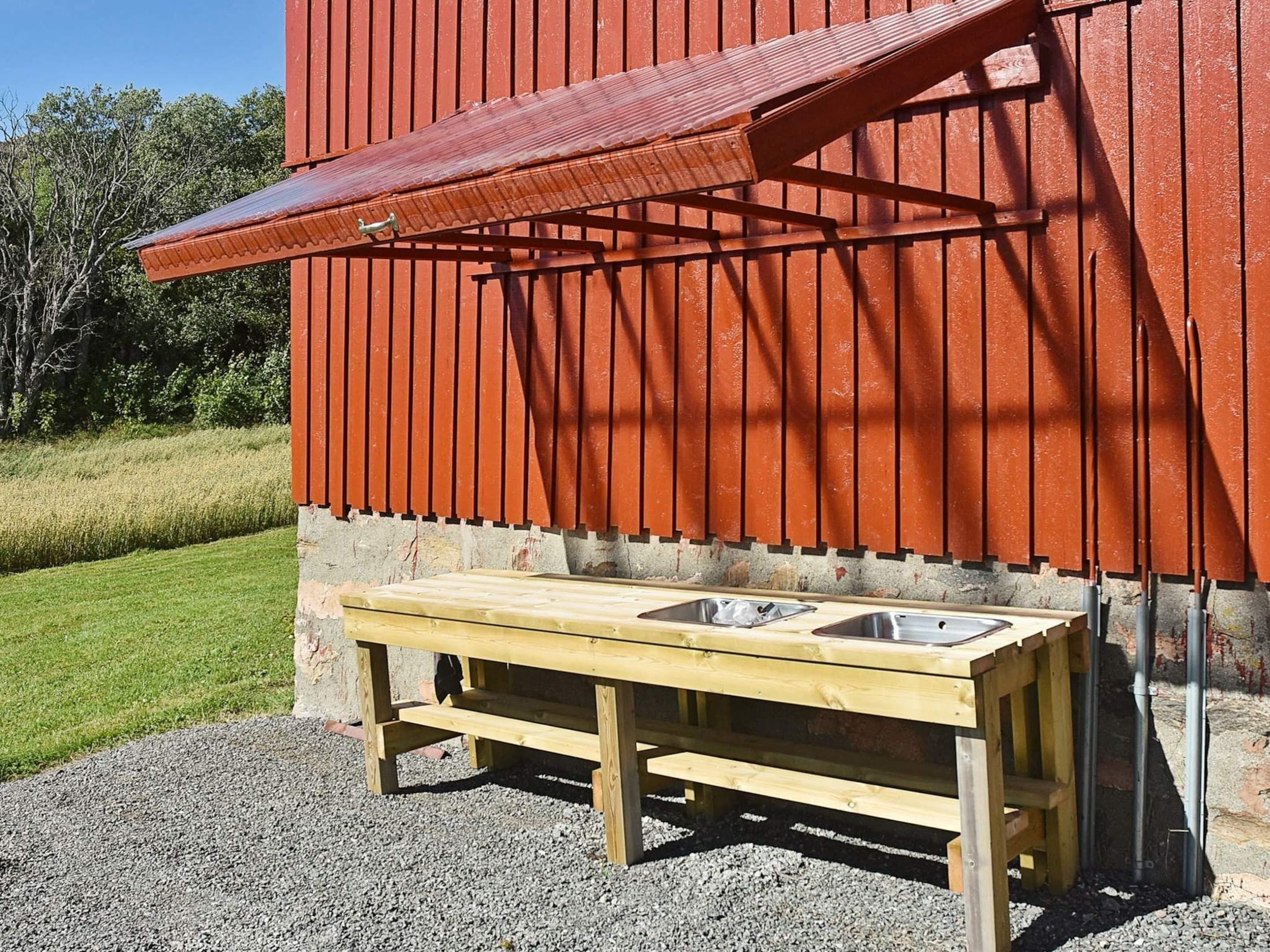 A wooden outdoor bench with two metal sinks, set against a red building with a corrugated metal awning.