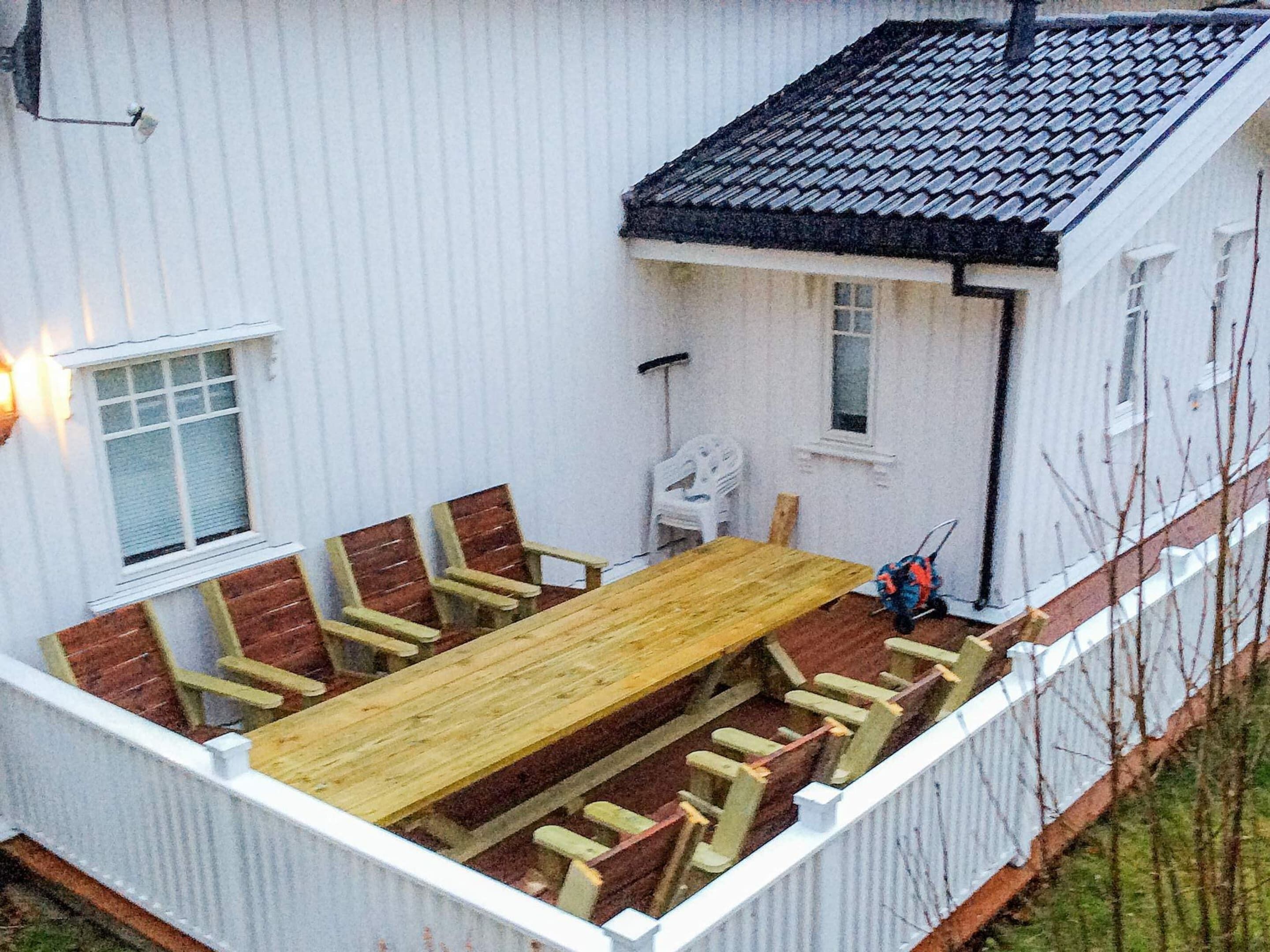 A white building with a tiled roof, a wooden deck, and a dining table with chairs.