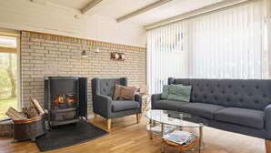 A modern living room with a brick wall, a fireplace, two armchairs, a sofa, and a glass coffee table. - 6 Person Holiday Home in Hurup Thy-by Traum (Hurup Thy)