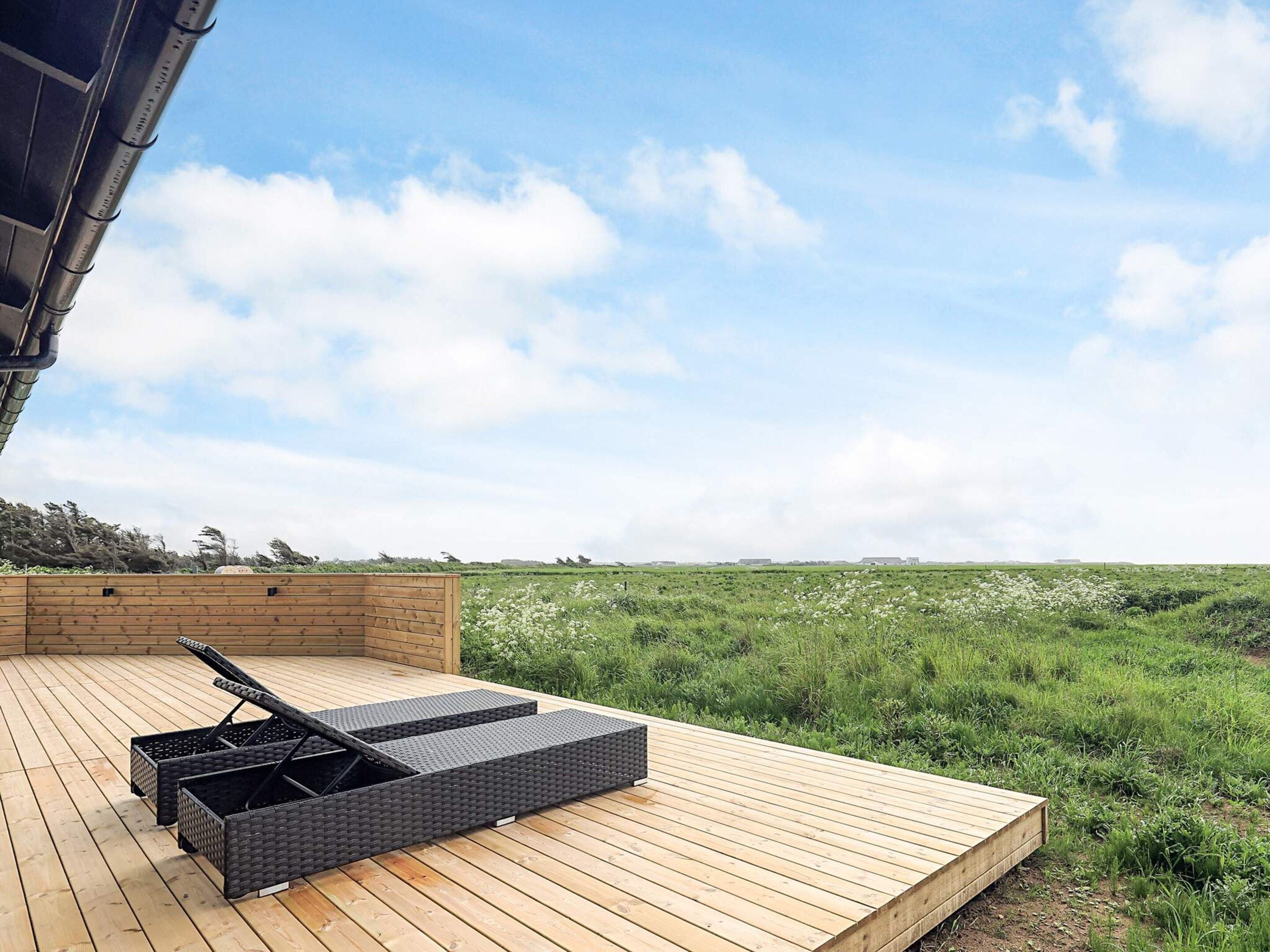 A wooden deck with a black wicker lounge chair and a small table.