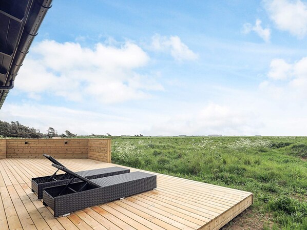 A wooden deck with a black wicker lounge chair and a small table.