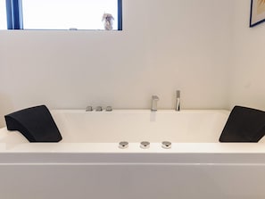 A modern bathroom with a white bathtub, two black bathmats, and a window above the tub. - 5 Star Holiday Home in Lokken (Lokken)