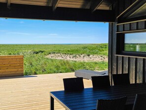 A wooden deck with a table and chairs, overlooking a grassy field and a clear sky. - 5 Star Holiday Home in Lokken (Lokken)