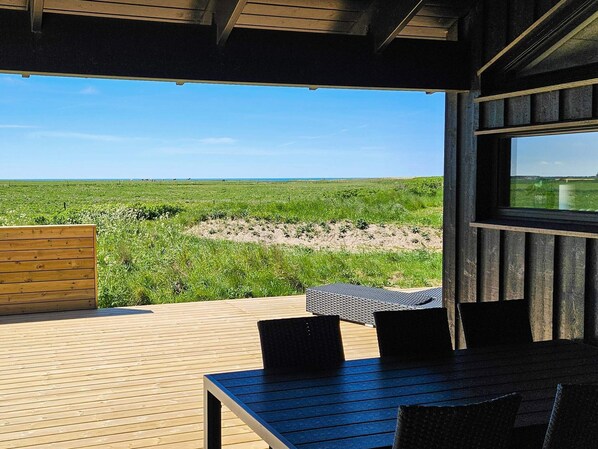 A wooden deck with a table and chairs, overlooking a grassy field and a clear sky.