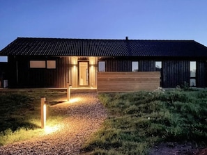 A modern building with a sloped roof, wooden exterior walls, and a gravel pathway leading to the entrance.