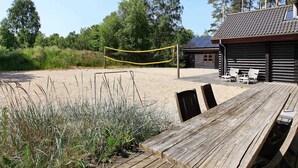 Une terrasse en bois avec des sièges extérieurs, un filet de volley-ball et un chalet équipé de panneaux solaires.