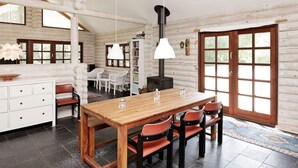 L’intérieur d’une cabane en rondins, avec une table à manger en bois, des chaises, un buffet blanc et une cheminée.