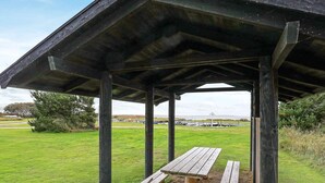 A wooden pavilion with benches in a grassy field, overlooking a beach with boats. - 6 Person Holiday Home in Vemb (Vemb)