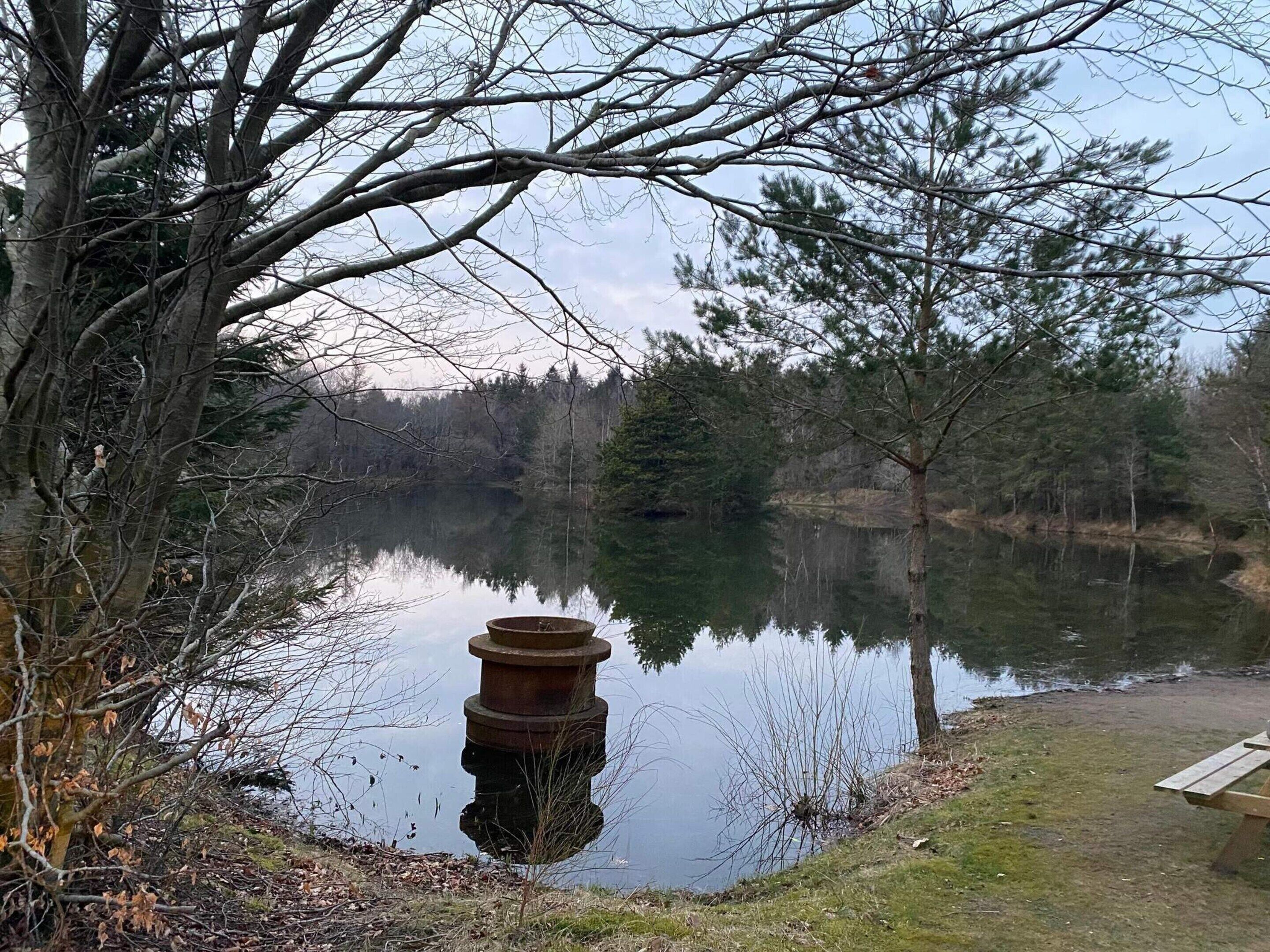 Ein ruhiger See mit einem hölzernen Steg und einer Metallkonstruktion im Wasser.