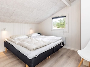 A bedroom with a bed, bedside table, lamp, window, and a chair.