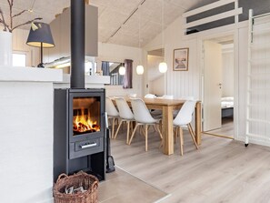 A modern interior with a wood-burning stove, a dining area with chairs, and a white door leading to another room. - 4 Star Holiday Home in Bindslev (Bindslev)