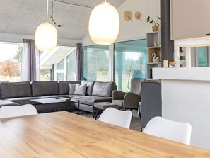 A modern living room with a sectional sofa, a wooden dining table, and pendant lighting. - 4 Star Holiday Home in Bindslev (Bindslev)