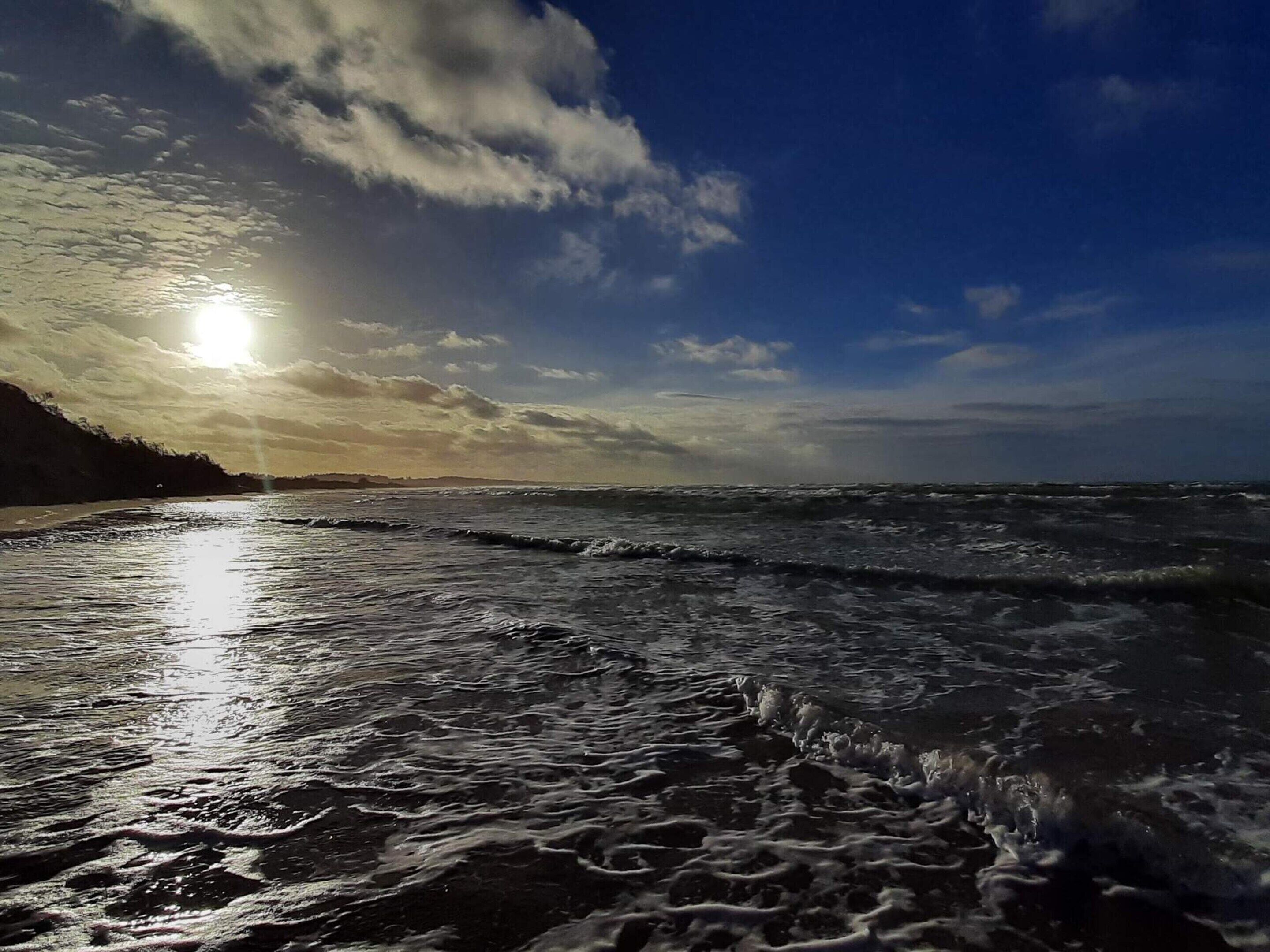 Una playa con olas, cielo despejado y el sol poniéndose o saliendo.