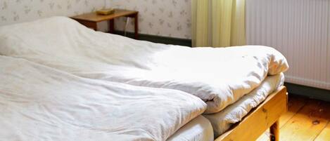 A single bed with a wooden frame in a room with floral wallpaper and a radiator.
