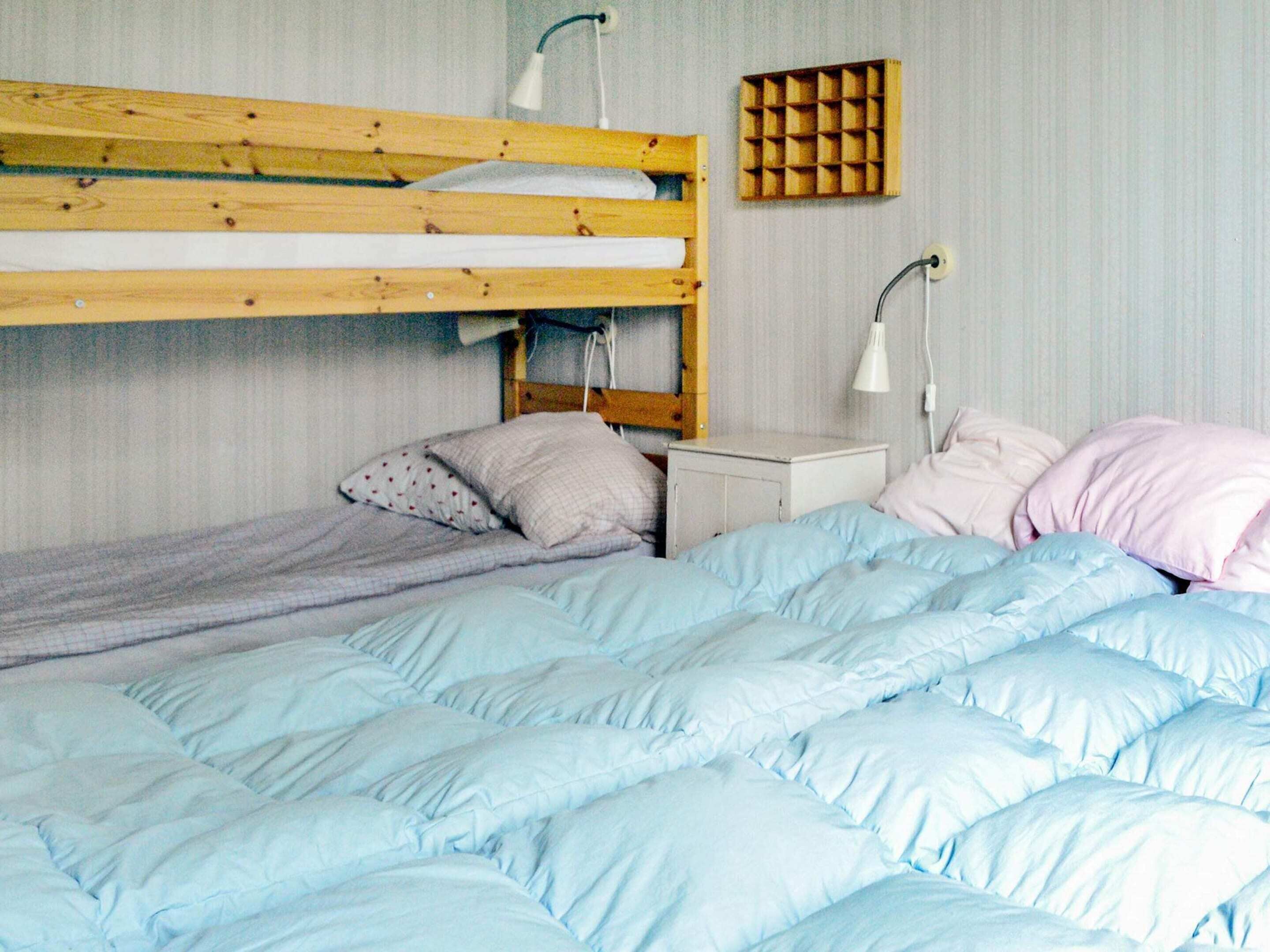 A bunk bed with a wooden frame, a bedside table with a lamp, and a wall-mounted storage unit.