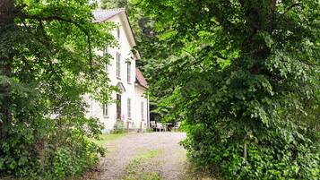 A pathway leading to a white building with multiple windows, surrounded by lush greenery.