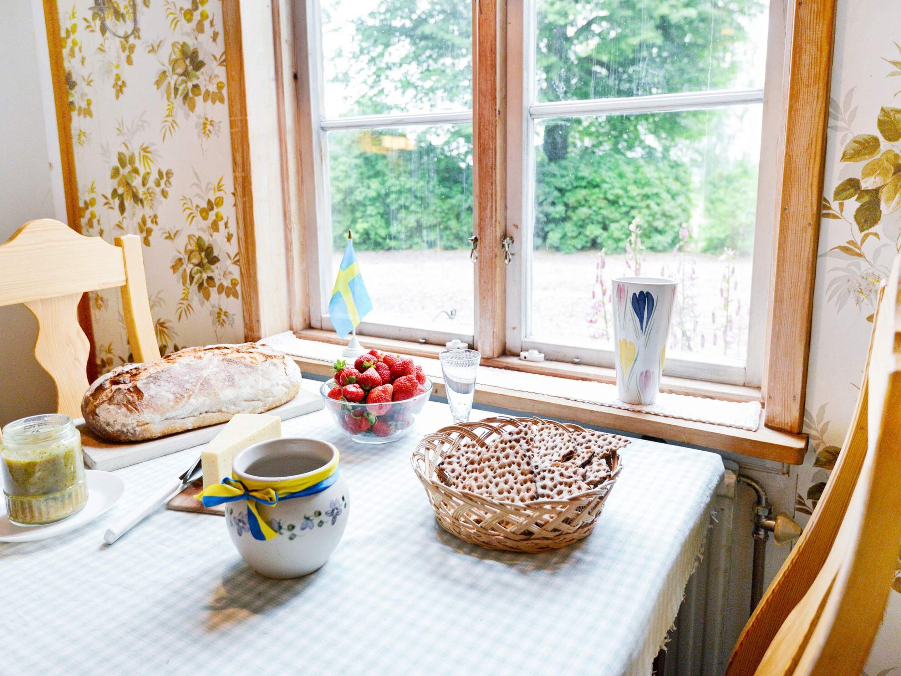 A table with bread, strawberries, a bowl of berries, a cup, and a basket of crackers by a window with a flag.