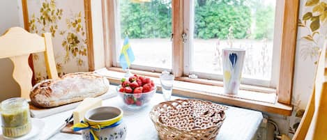 A table with bread, strawberries, a bowl of berries, a cup, and a basket of crackers by a window with a flag.