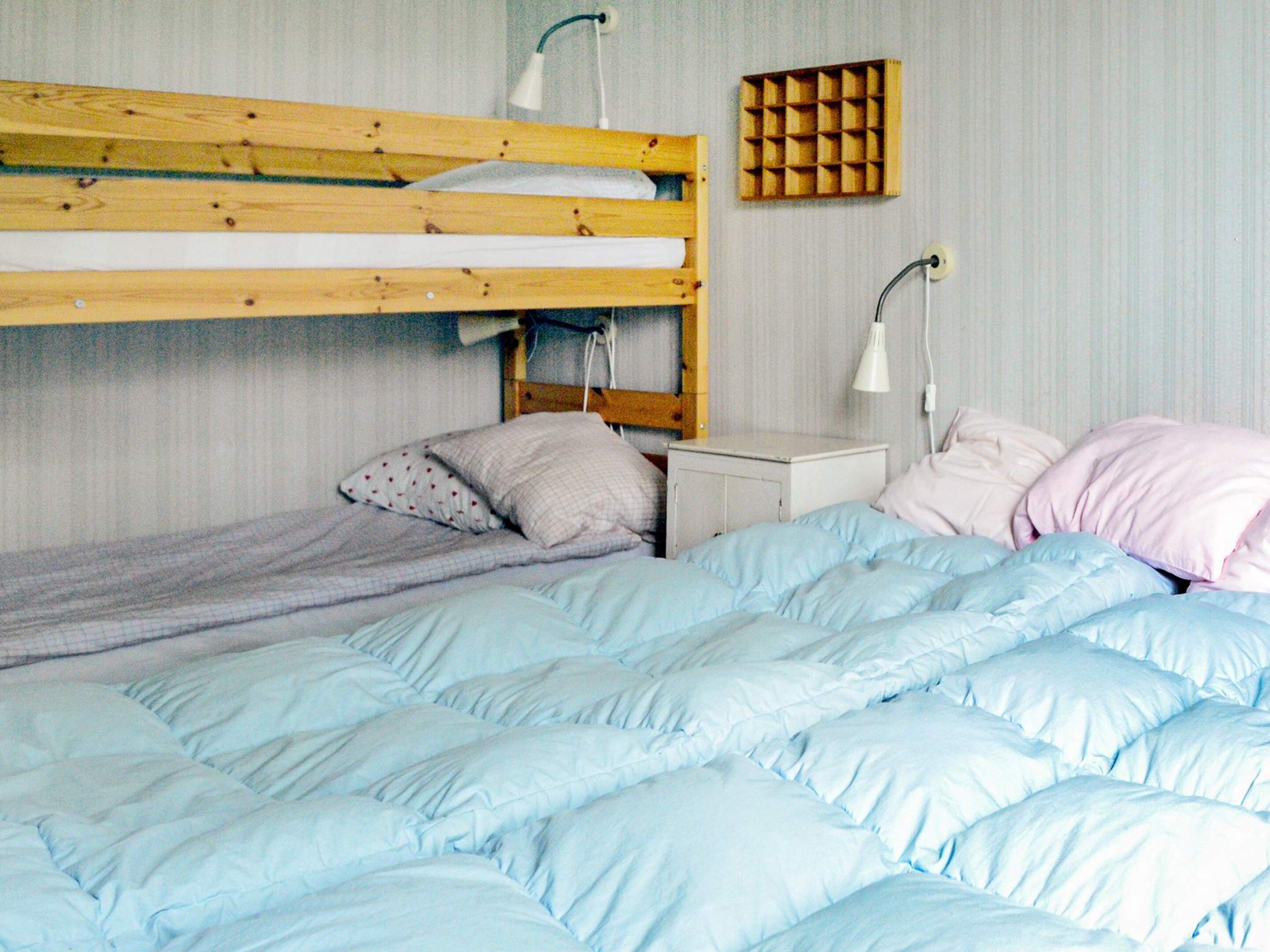 A bunk bed with a lower bunk, a bedside table, a lamp, and a wall-mounted storage unit.