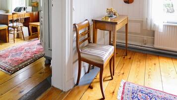 Una habitación con piso de madera, una silla a rayas, una pequeña mesa con un florero y un violín en la pared.