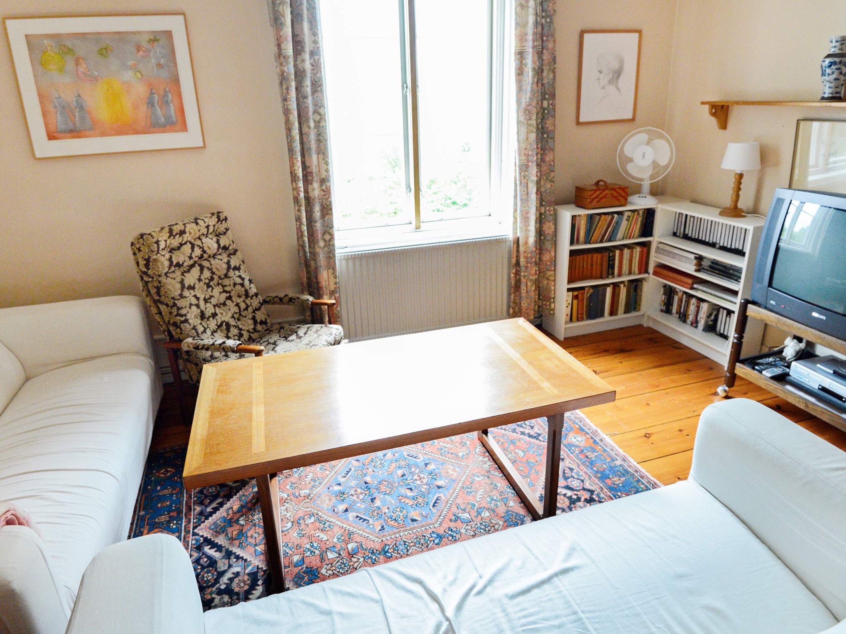 Un salon comprenant un canapé, un fauteuil, une table, une bibliothèque et un téléviseur.